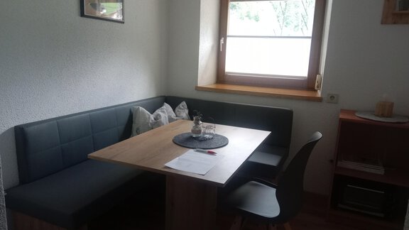 A cozy dining area with a table and a bench. There is a view of a window and some decorative elements. - Gästehaus Sternberger - Sölden