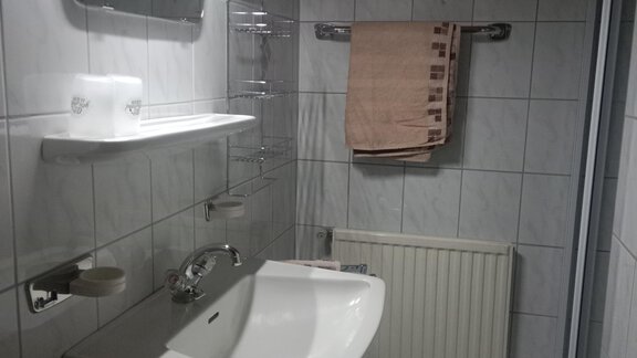 A modern bathroom with white tiles and a sink. A towel hangs on the wall, and there is a mirror as well as a heater. - Gästehaus Sternberger - Sölden