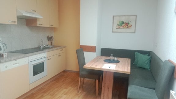 A modern kitchen with wooden floors and bright furnishings. The dining area consists of a table and a bench with chairs. - Gästehaus Sternberger - Sölden