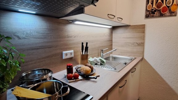 A modern kitchen with light wooden furniture and a countertop. Pots are on the stove, and fresh ingredients are clearly visible. - Gästeheim Schmiedhof - Sölden