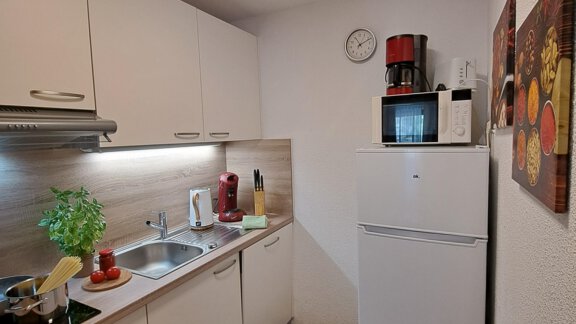 A modern kitchen with white cabinets and a wooden surface. In the room, there is a refrigerator, a sink, and some kitchen utensils. - Gästeheim Schmiedhof - Sölden