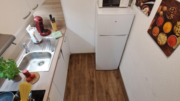 A small, modern kitchen with wooden flooring. The equipment includes a refrigerator, a coffee machine, and some kitchen utensils. - Gästeheim Schmiedhof - Sölden
