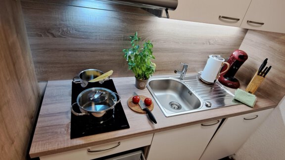 A modern kitchen with a stove, a sink, and a drawer full of cutlery. Fresh ingredients and kitchen appliances are on the countertop. - Gästeheim Schmiedhof - Sölden