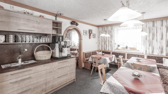 A cozy kitchen with wooden shelves and tables. The room is bright and inviting, with a large window. - Gästeheim Schmiedhof - Sölden