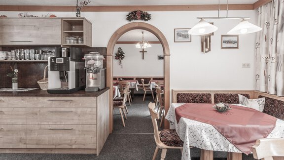 A cozy inn with wooden furniture and a round table. In the background, tablecloths and chairs can be seen waiting for the guests. - Gästeheim Schmiedhof - Sölden