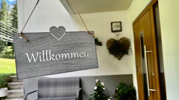 An inviting entrance sign with the inscription "Welcome" hangs on a wall. Nearby, there are plants and a chair that create a friendly atmosphere. - Gästeheim Schmiedhof - Sölden