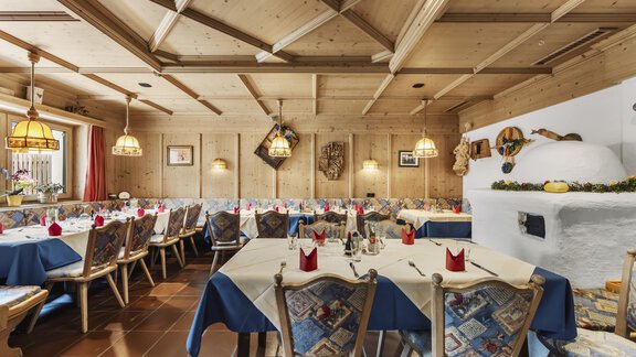 A cozy restaurant with wooden ceilings and stylish lamps. The tables are set with blue tablecloths and red napkins. - Gasthof Granstein - Sölden