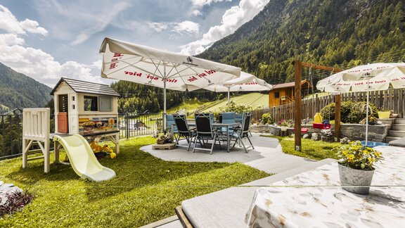 A beautiful garden with a playground and a dining table under sunshades. The surrounding mountains and the good weather create an inviting atmosphere. - Gasthof Granstein - Sölden