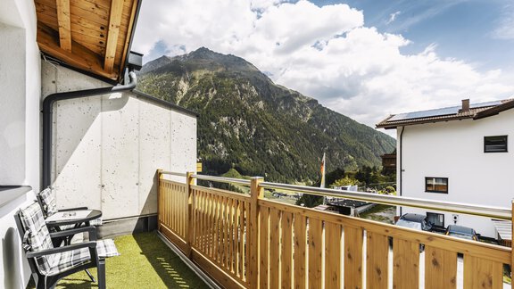 A balcony with wooden railing and chairs. In the background, majestic mountains and a clear sky can be seen. - Gasthof Granstein - Sölden