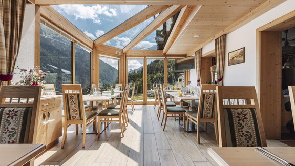 A bright room with wooden furniture and large windows. The view shows a picturesque landscape with mountains and clouds. - Gasthof Granstein - Sölden