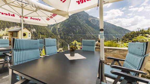 A cozy terrace with modern chairs and a table. In the background, majestic mountains and a blue sky can be seen. - Gasthof Granstein - Sölden