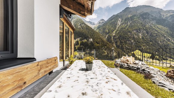 A modern terrace with a view of the mountains. The floor is decorated with a decorative pattern, and there is a pot with plants on the table. - Gasthof Granstein - Sölden