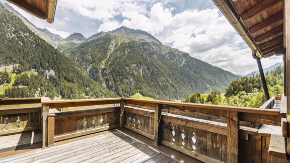 A beautiful balcony with a wooden railing and a view of the majestic mountains. The sky is partly cloudy and the landscape is green and inviting. - Gasthof Granstein - Sölden