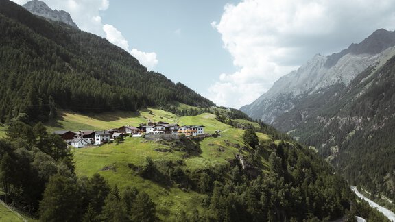 A picturesque valley with green meadows and a small village nestled between the mountains. The clouds drift across the sky and nature is lush and inviting. - Gasthof Granstein - Sölden