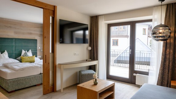 Ein modernes Hotelzimmer mit einem Doppelbett, Fernseher und einem Schreibtisch. Große Fenster lassen viel Tageslicht herein und bieten einen Blick nach draußen. - Glanz & Glory Hotel - Sölden