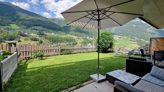 A cozy outdoor area with a lounging space and a parasol. In the background, green hills and a blue sky stretch out. - Granbichlhof - Sölden