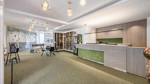 A modern foyer with a reception desk and a cozy seating area. The walls are brightly designed and the lighting creates an inviting atmosphere. - GREEN.Apartments by Camping Sölden - Sölden