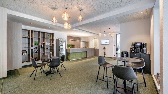A modern office with a cozy lounge area. There are tables, chairs, and a kitchenette in the background. - GREEN.Apartments by Camping Sölden - Sölden