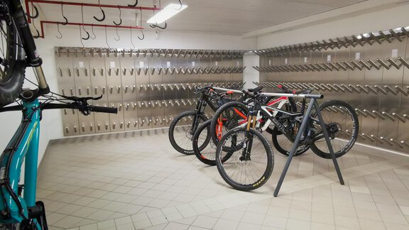 A modern bike storage room with several bicycles on a rack. Hooks are present on the wall for hanging additional bikes. - GREEN.Apartments by Camping Sölden - Sölden