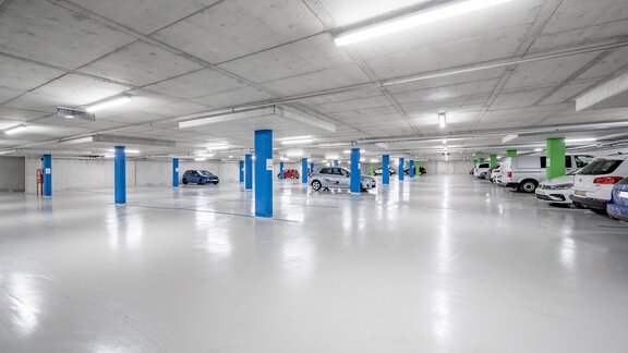 An empty parking space with bright walls and several cars. The pillars are painted blue and green. - GREEN.Apartments by Camping Sölden - Sölden
