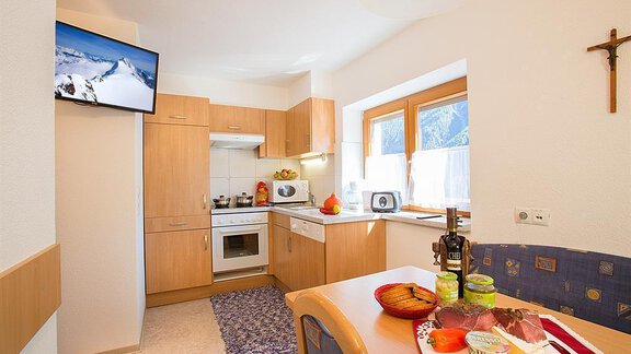 A bright and cozy kitchen with modern appliances and wooden furniture. Fresh groceries are on the table, and a television is mounted on the wall. - Haus Alois - Sölden