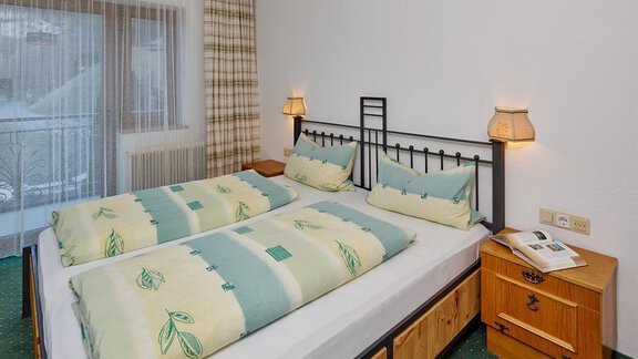 A cozy bedroom with two single beds and a wooden dresser. Daylight streams in through the window, and the walls are designed in light colors. - Haus Am Hang - Sölden