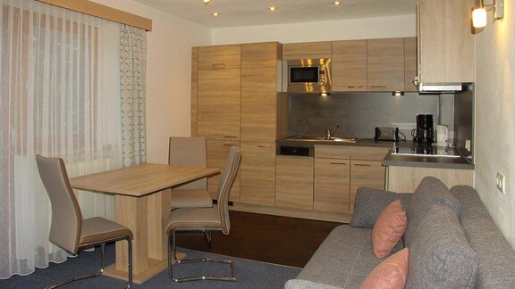 A modern kitchen with a dining table and chairs. The living area is cozy with a gray sofa and natural wood elements. - Haus am Wildbach - Sölden