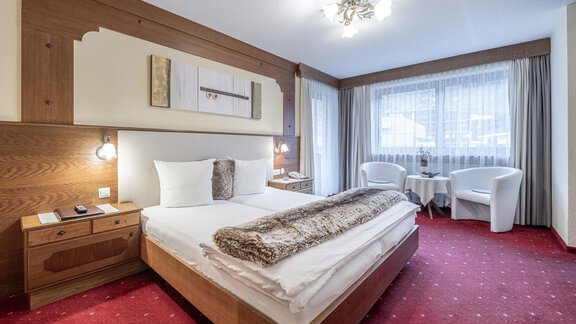 A cozy hotel room with a double bed and a modern design. The space is bright and inviting, with a table and chairs next to a large window. - Haus Amaris - Sölden