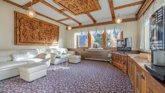 A cozy living room with elegant furniture and ornate wooden walls. Large windows provide plenty of natural light and a view outside. - Haus Amaris - Sölden