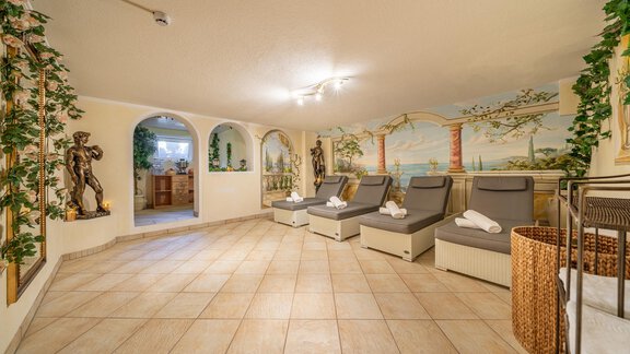 A relaxing wellness area with comfortable loungers and decorative wall paintings.  
Green plants and soft lighting create a calming atmosphere. - Haus Amaris - Sölden