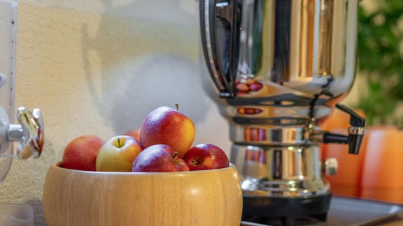 A bowl of fresh apples is next to a shiny kettle. In the background, some colorful mugs can be seen. - Haus Amaris - Sölden
