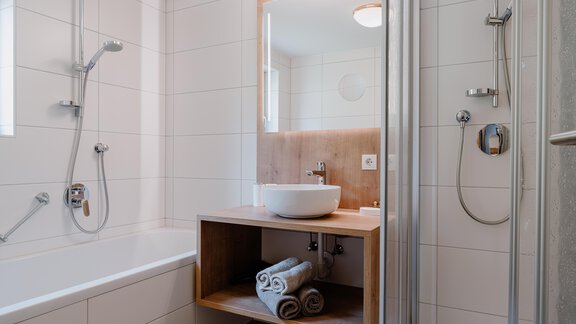 A modern bathroom with a bathtub and a shower. Several towels are ready on a wooden shelf. - Haus Crystal - Sölden
