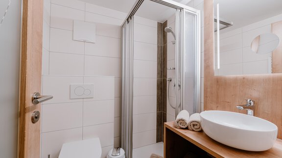 A modern bathroom with a shower and sink. There are towels on a wooden shelf and bright, neutral colors. - Haus Crystal - Sölden