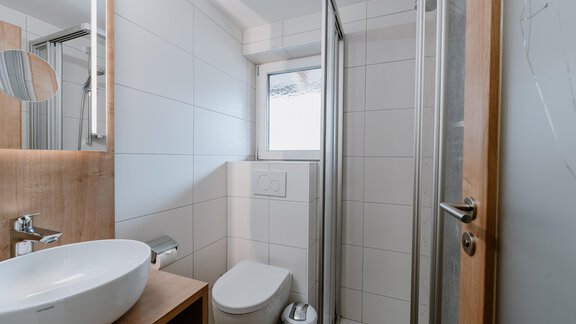 A modern bathroom with a shower, a sink, and a toilet. The walls are tiled and the light is bright. - Haus Crystal - Sölden