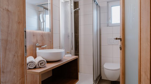 A modern bathroom with a shower and a sink. It is bright and minimally designed, featuring wood and tile elements. - Haus Crystal - Sölden