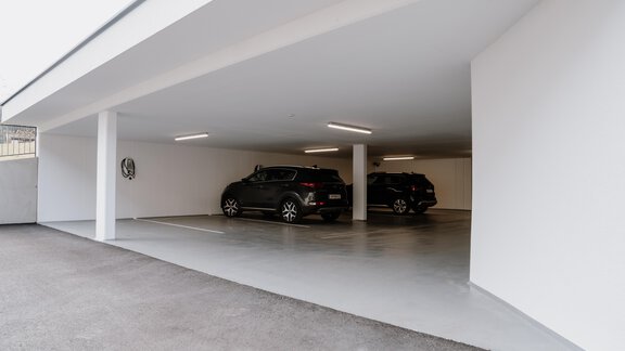 A modern underground parking garage with bright walls and two parked cars. The lighting creates a friendly atmosphere. - Haus Crystal - Sölden