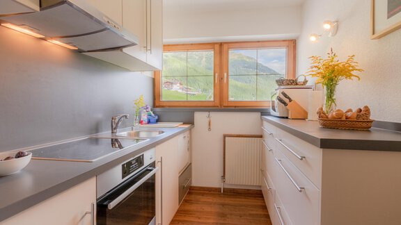 A modern kitchen with bright cabinets and a large window. Fresh flowers and baked goods are arranged on the countertop. - Haus Edmund - Sölden