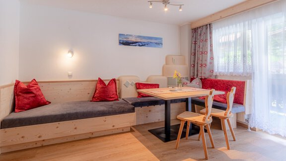 A cozy dining area with a wooden sofa and a table. Red cushions and plenty of light create an inviting atmosphere. - Haus Edmund - Sölden