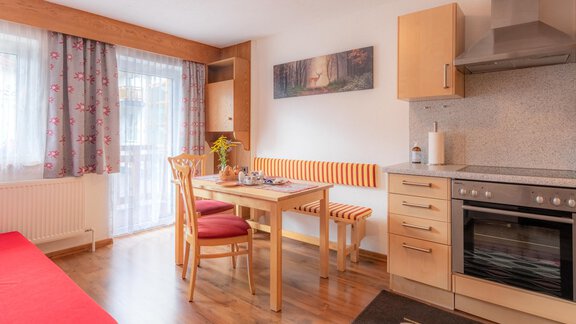 A bright kitchen corner with a table, chairs, and a sofa. Daylight is streaming in through the window, and the walls are painted in warm colors. - Haus Edmund - Sölden
