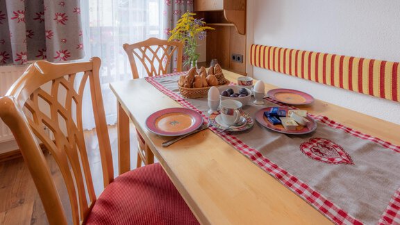 A cozy dining table with wooden chairs and a set breakfast. On the table are plates, cups, and sweet pastries. - Haus Edmund - Sölden
