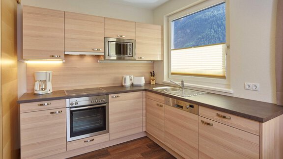 A modern kitchen with wooden cabinets and elegant appliances. The window offers a view of the mountains. - Haus Fridolin - Sölden