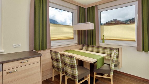A cozy dining area with a table and striped chairs. Large windows provide plenty of daylight and a view outside. - Haus Fridolin - Sölden