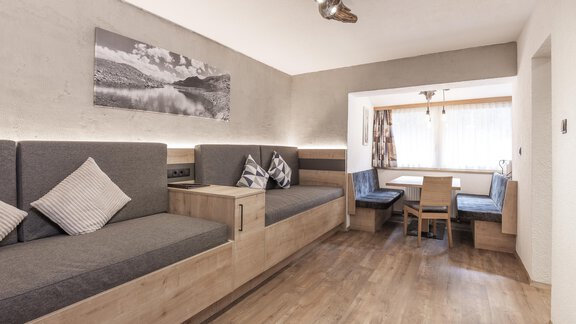 A modern living room with comfortable seating and a dining area. The walls are light and there are large windows that let in plenty of light. - Haus Manfred - Sölden