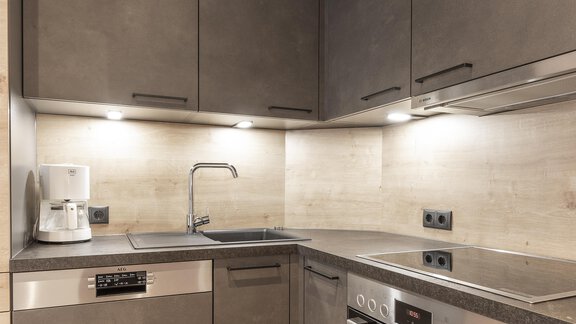 A modern kitchen with gray cabinets and stainless steel appliances. The lighting creates a cozy atmosphere. - Haus Manfred - Sölden