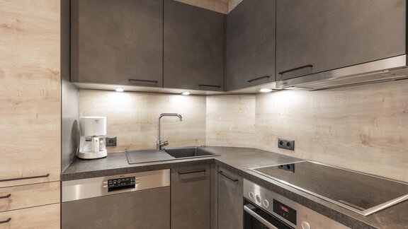 A modern kitchen with dark cabinets and a functional layout. The room is well-lit and includes appliances such as a kettle and a stove. - Haus Manfred - Sölden