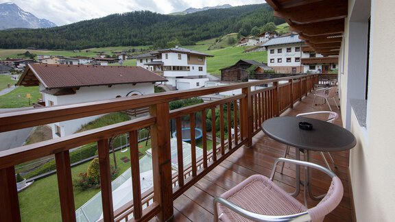 A balcony with a wooden railing overlooking green meadows and traditional chalets. In the background, the mountains and a cloudy sky can be seen. - Haus Montjola - Sölden