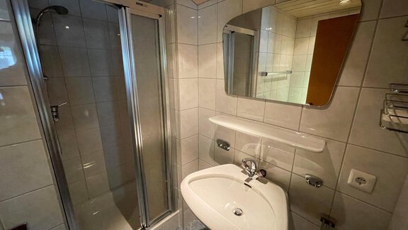 A modern bathroom with a shower and sink. The walls are tiled with light tiles and a mirror is available. - Haus Nesselhof - Sölden