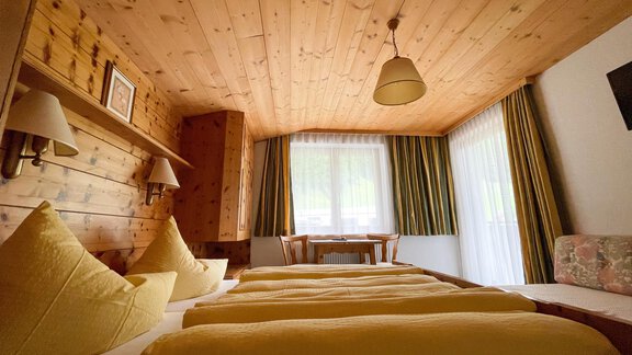 A cozy room with wooden walls and a wooden ceiling. There are large windows, two beds with yellow pillows, and a table with chairs. - Haus Nesselhof - Sölden