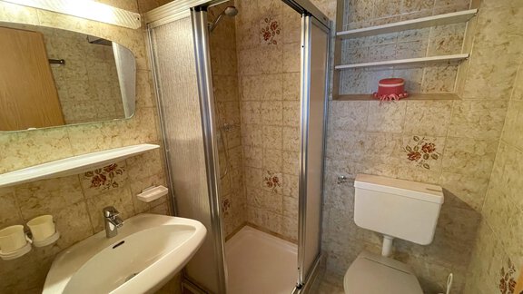 A small bathroom with a shower, sink, and toilet. The walls are decorated with tiles and floral patterns. - Haus Nesselhof - Sölden