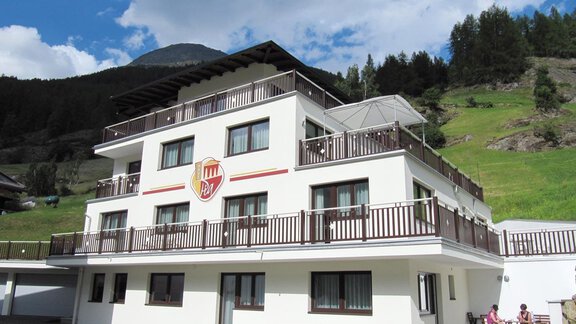A modern building with several floors and balconies. In the background, green mountains and a blue sky can be seen. - Haus PIA by A CASA - Sölden